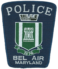 The patch of the Bel Air, Maryland, Police Department prominently features the coat of arms of the town it serves. The crenellated mural crown at the top represents Bel Air’s sovereignty as the county seat of Harford County, while the five merlons symbolize the town’s five-commissioner form of government. The green shield in the center denotes the fertile fields of the county, with the tower in the middle symbolizing the town. The two silver pales on either side of the tower represent Bel Air’s location between the silvery waters of Winters Run to the west and Bynum Run to the east. The banner at the bottom marks the year the town was incorporated and the Bel Air Police Department was founded. 