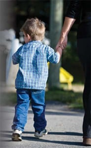 A child is pictured walking through a playground, guided by a parent, guardian, or perhaps stranger.