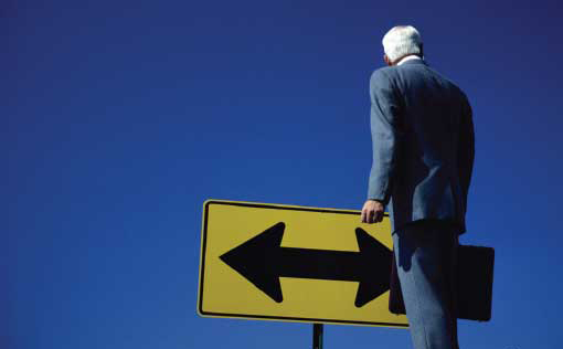 Businessman Standing in Front of Road Sign with Two-Directional Arrow (Stock Image)