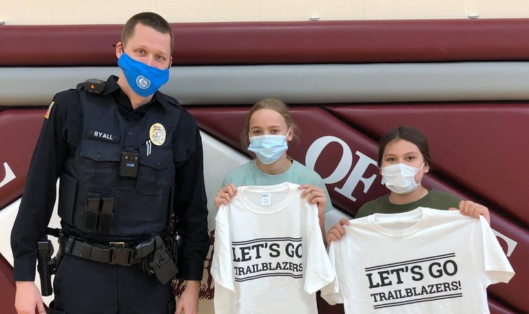 An image of a Torrington officer with two young girls holding t-shirts from the Caught Doing Something Right youth program.