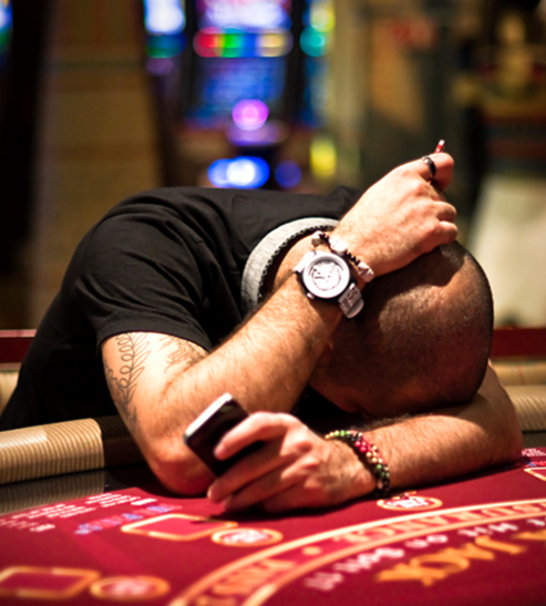 An obsessive gambler rests his head on a black jack table having lost all his money.