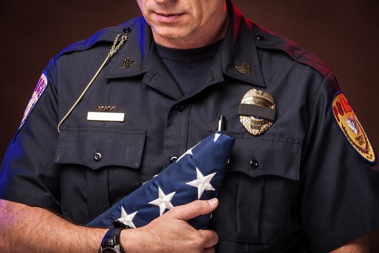 A stock image of a police officer holding a folded American flag.