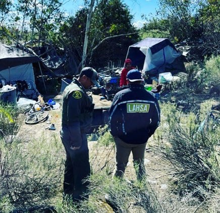 An image of deputies assigned to the Los Angeles County Sheriff’s Department’s Homeless Outreach Services Team and Mental Evaluation Team are joined by the Los Angeles Homeless Services Authority at a homeless camp site.