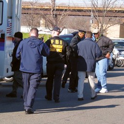 FBI Terrorism Task Force member and other law enforcement personnel outside an official vehicle. 