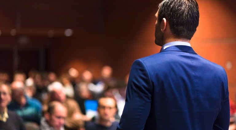 Stock photo portraying a business man giving a speech in front of an audience