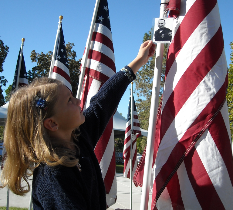 An image of a young girl pinning a photo of an officer on a flag police at the annual Utah Law Enforcement Memorial service.