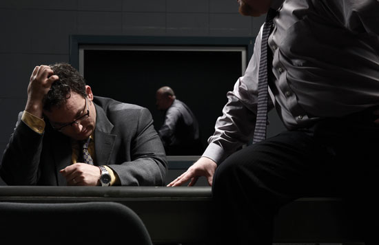A police detective speaks with a suspect in an interrogation room.