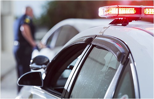 Stock image of a police officer standing next to a car he has pulled over.