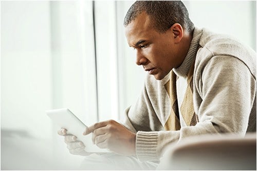 Stock image of a father sitting on a couch looking at a computer tablet.