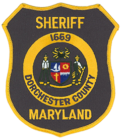  Dorchester County, Maryland, was founded in 1669 on the Eastern Shore of the Chesapeake Bay. The county’s government seal, depicted on the service patch of the Dorchester County Sheriff’s Office, includes a crab at the top, a waterman on the left, and a farmer on the right. These represent the county’s two main sources of income: fishing and farming. Clockwise from the top left, the center shield depicts a sailboat, a cog, a display of the water and sky, and a cross. These items reflect the county’s association with water sports; industry; the waterways that surround it; and, dating back to its founding, the Roman Catholic Church.