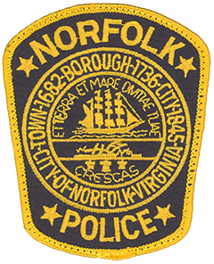 The patch of the Norfolk, Virginia, Police Department prominently depicts the Seal of the City of Norfolk. Adopted in 1913 the seal’s outer border gives a brief history of Norfolk’s evolution from a town in 1682 to a borough in 1736 and then a city in 1845. The top half of the inner circle consists of a ship under full sail, typifying maritime commerce and the city’s rich naval history. The bottom half depicts a field with a plow and three sheaves of wheat, representing agriculture. The Latin motto bordering the circle reads “Et terra et mare divitiae tuae crescas,” which translates as “May you increase your wealth on land and sea.”