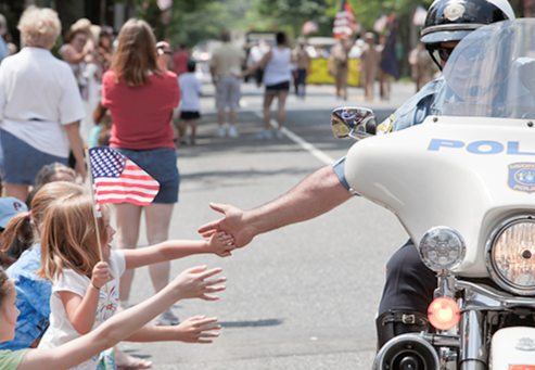 A police officer on a motorcycle reaches out waving kids at a community parade.
