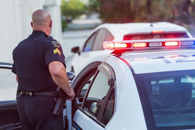 A stock image of a police officer approaching a vehicle he has pulled over.
