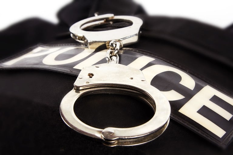 A stock image of a police vest with a set of handcuffs laying on top.