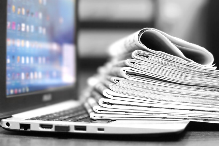 A stock image of a computer and newpapers.