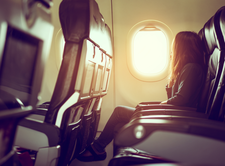A stock image of a female sitting alone on an airplane.