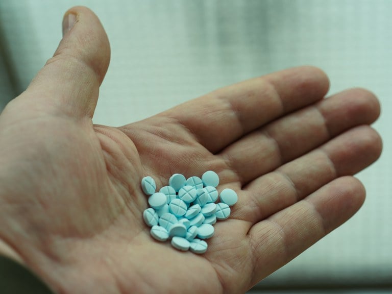 A stock image of a hand holding blue pills.