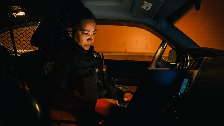A stock image of a police officer in their patrol car at night.