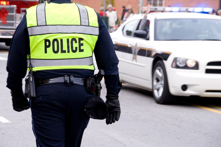 A stock image of a police officer near a police patrol car.