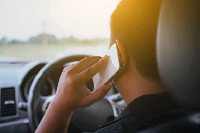 A stock image of a man in his vehicle talking on a cell phone. 