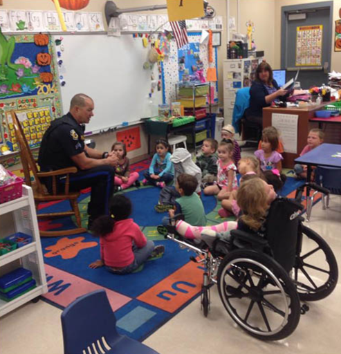 A school resource officer is shown interacting with grade school students in their classroom.