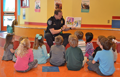 A School Resource Officer is depicted reading to the children he protects.